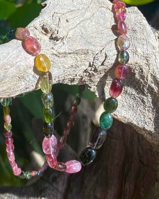 Smooth Tourmaline oval beads hand knotted necklace pink, yellow green  draped over a driftwood branch