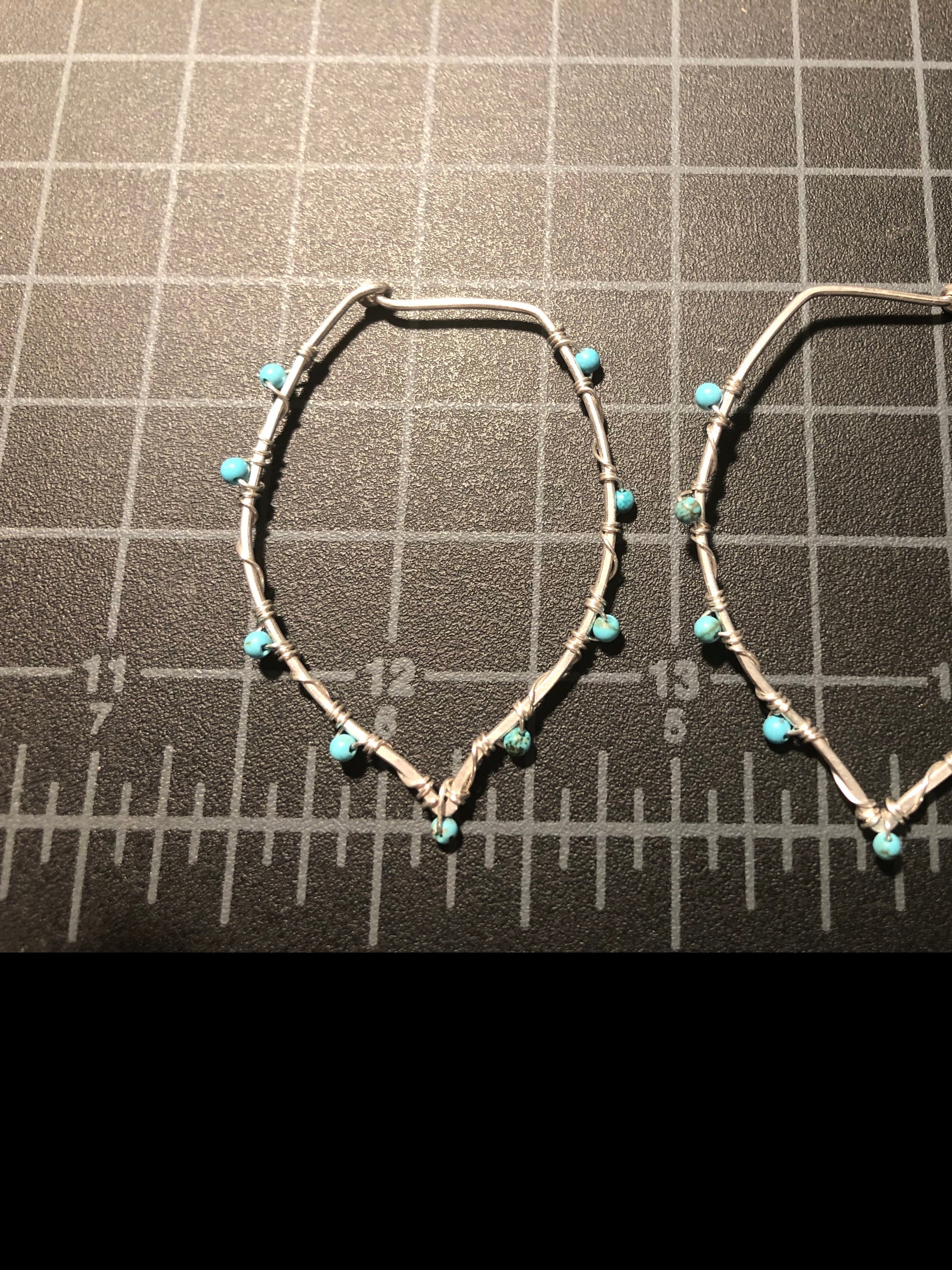 Silver leaf shape hoop earrings on a black mat with grid for measuring 